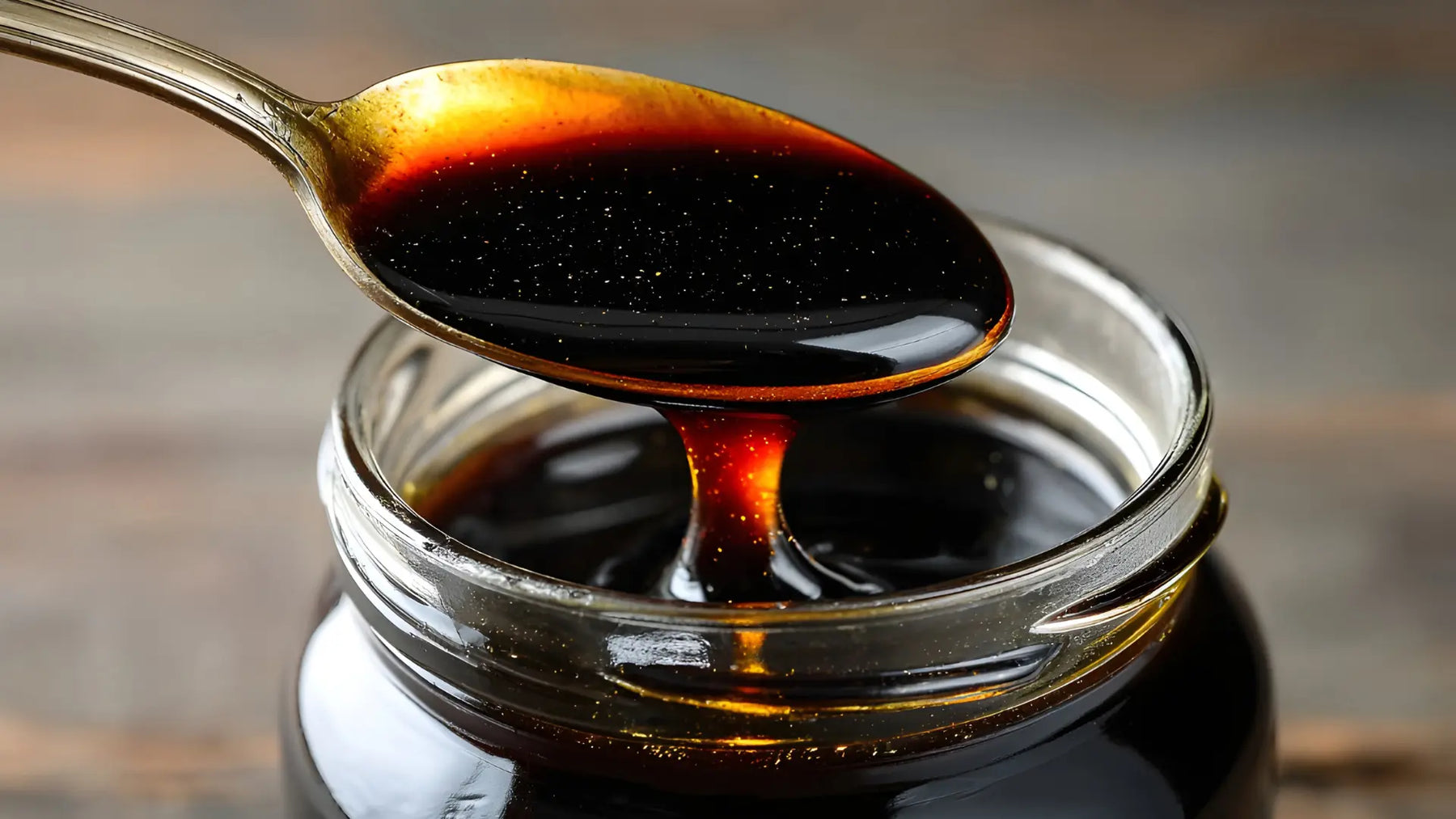 Glass jar of dark molasses with a wooden spoon dripping molasses on a kitchen counter
