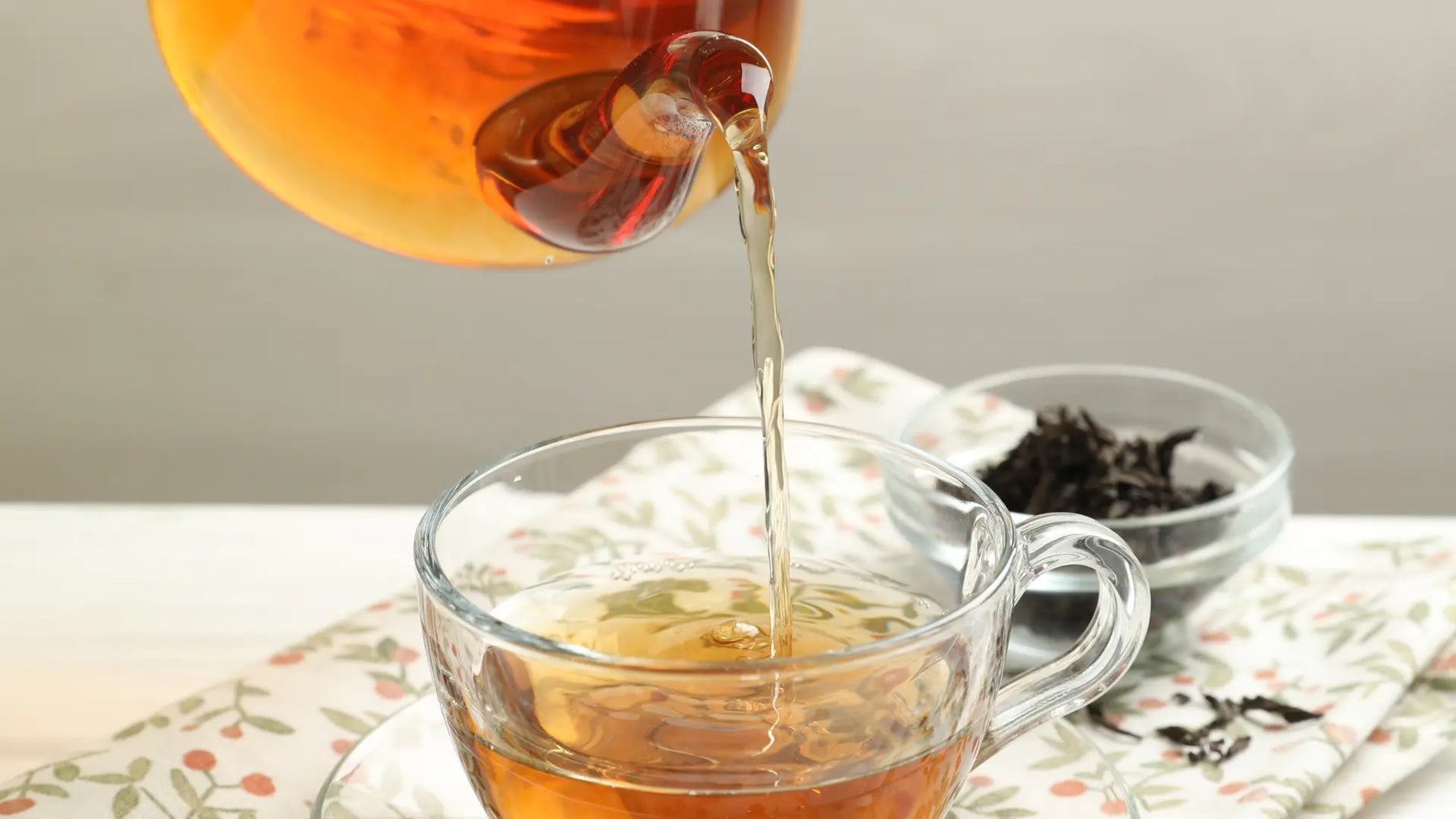 Cup of herbal essiac tea with a small pile of loose herbal blend on a neutral background