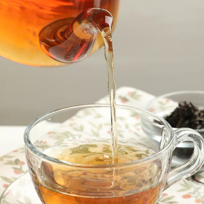 Cup of herbal essiac tea with a small pile of loose herbal blend on a neutral background