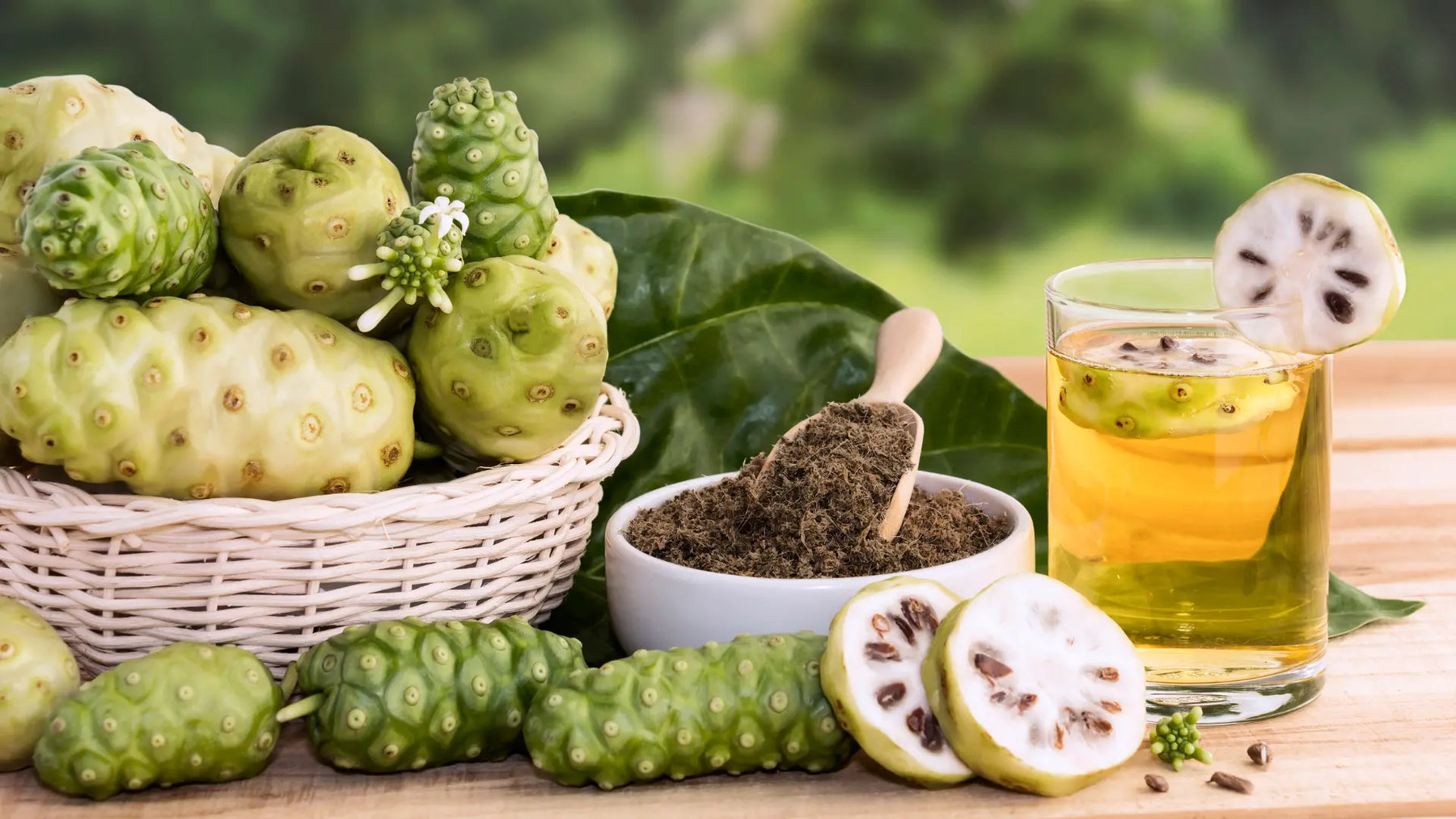 Bottle and glass of noni juice with noni fruit and green leaves on a natural wellness background