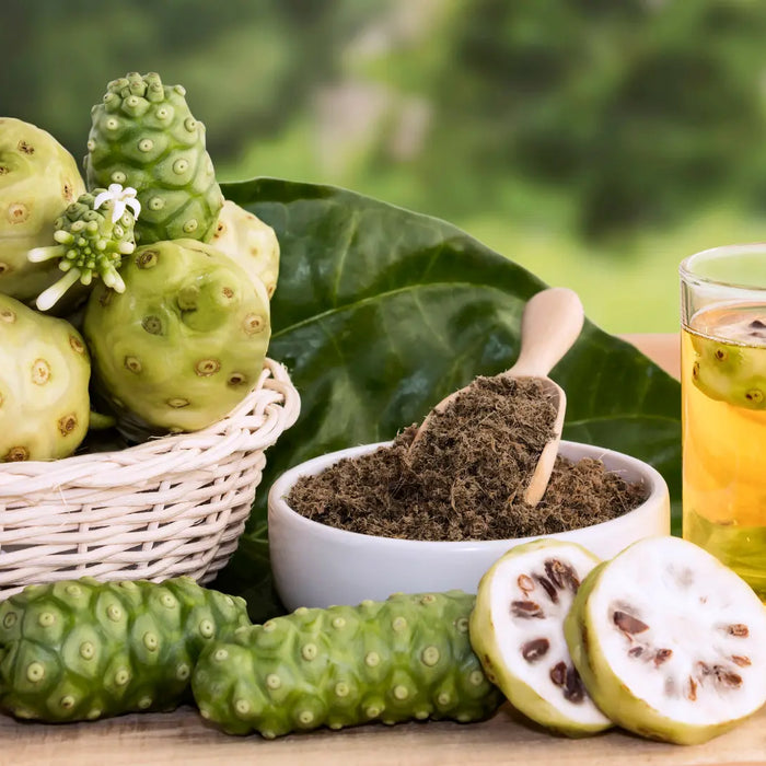 Bottle and glass of noni juice with noni fruit and green leaves on a natural wellness background