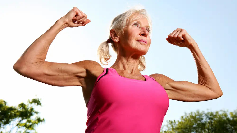 Woman in her 40s practising light dumbbell strength exercises at home, with a resistance band nearby in natural daylight.