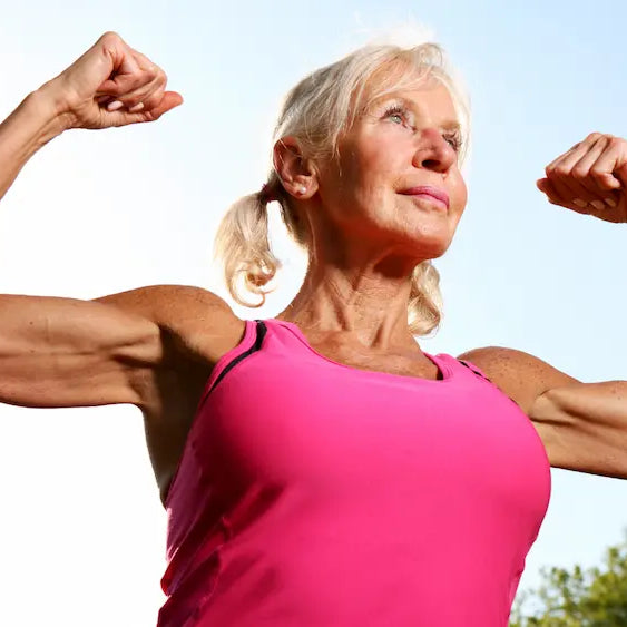 Woman in her 40s practising light dumbbell strength exercises at home, with a resistance band nearby in natural daylight.