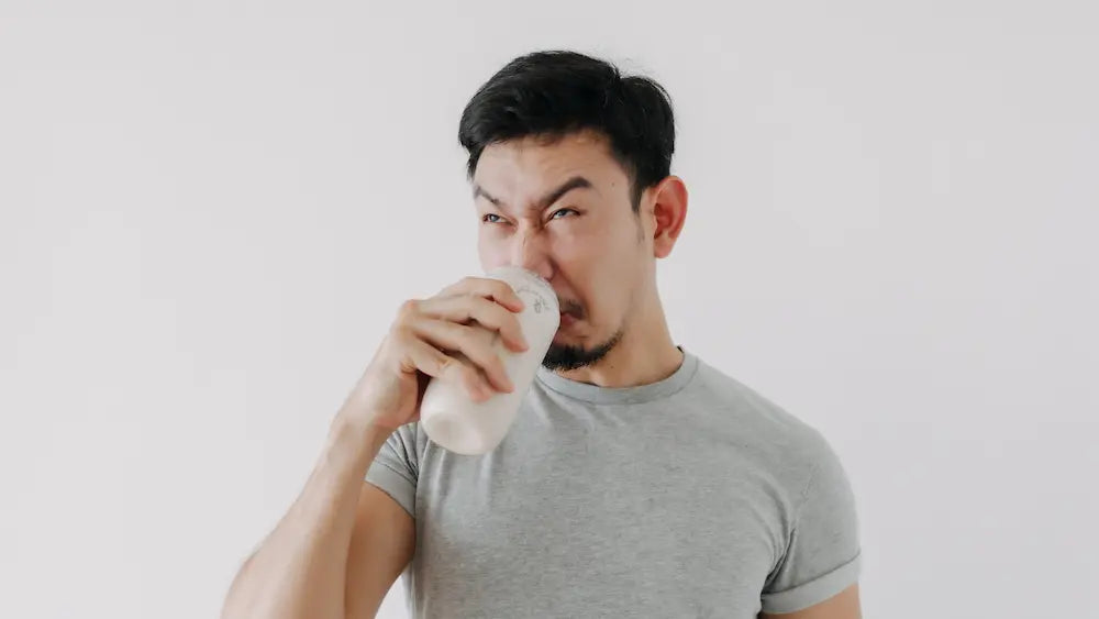 Clear glass of lightly lemon-coloured creatine drink beside a measured scoop of powder on a bright kitchen bench
