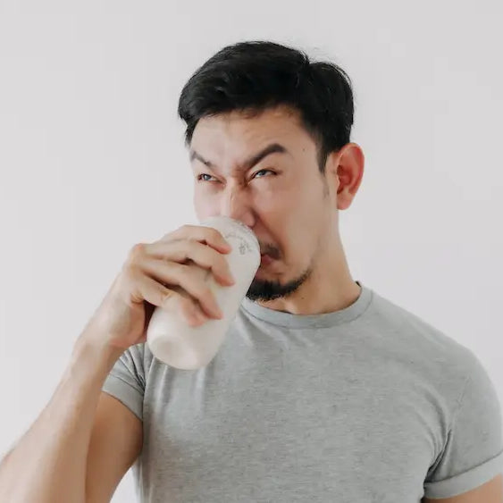 Clear glass of lightly lemon-coloured creatine drink beside a measured scoop of powder on a bright kitchen bench