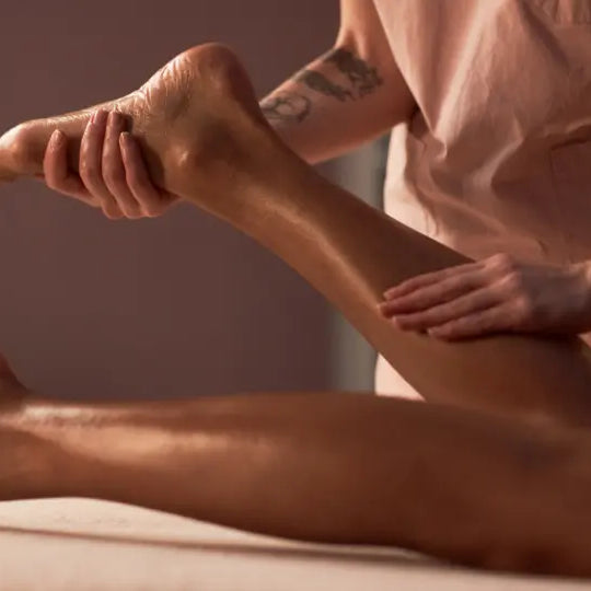 Adult preparing an emu oil massage with a pure oil bottle and balm-style warming rub nearby