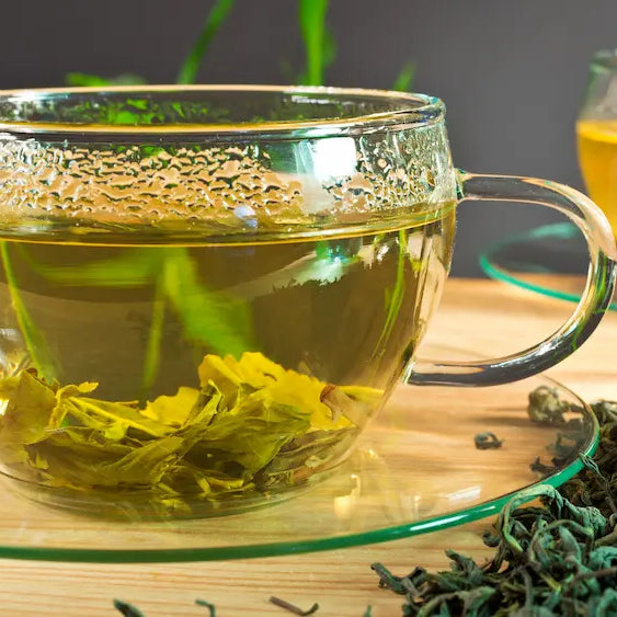 Brewed green tea, tea leaves and a green tea extract capsule arranged along a morning to afternoon routine