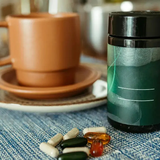 Liquid L-carnitine bottle with a measuring spoon beside a bottle of acetyl-L-carnitine capsules on a neutral surface.