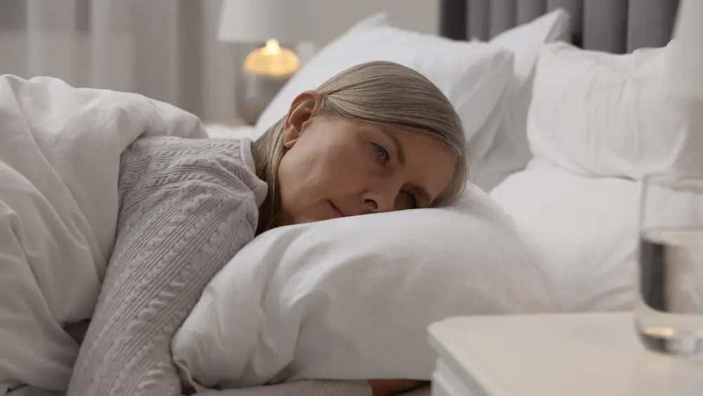 Midlife woman adjusting light bedding in a cool bedroom the morning after broken menopause sleep