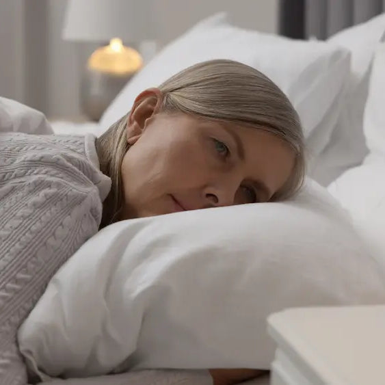 Midlife woman adjusting light bedding in a cool bedroom the morning after broken menopause sleep