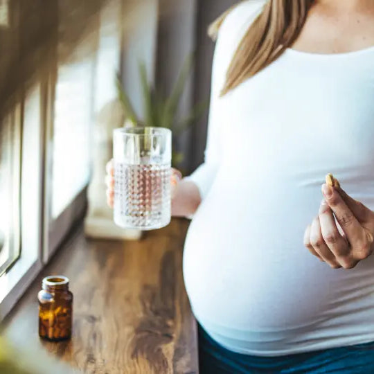 Pregnancy supplement bottles beside a handwritten prenatal vitamin label audit on a bright kitchen bench
