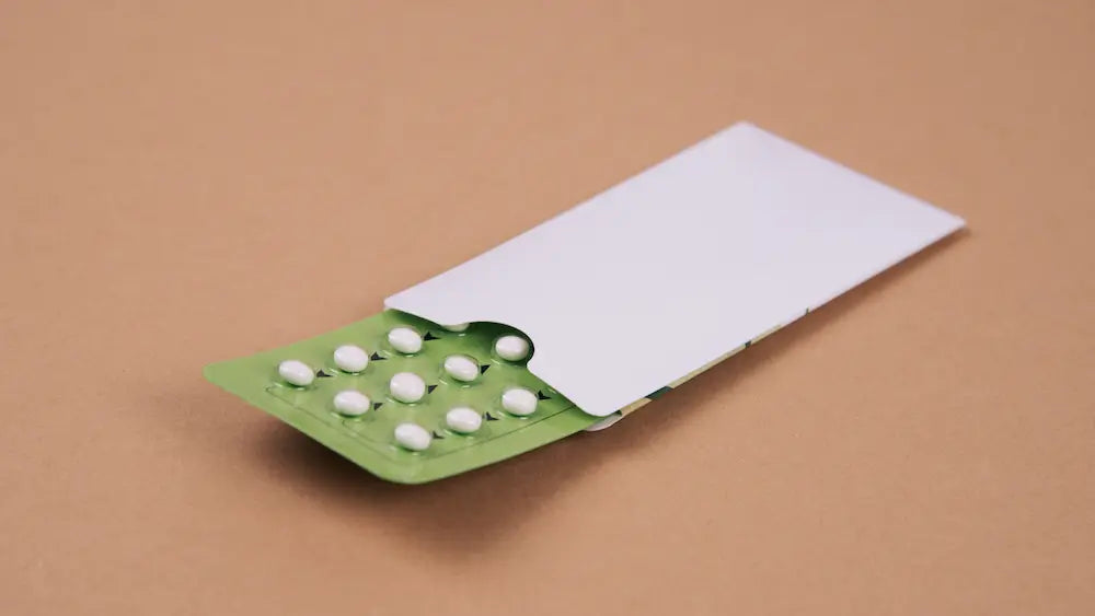 Closed contraceptive pill packet beside a prenatal supplement, notebook and water in a calm New Zealand home.