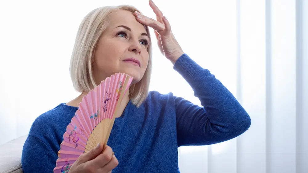 New Zealand woman cooling down beside an open window with iced water during a menopausal hot flush