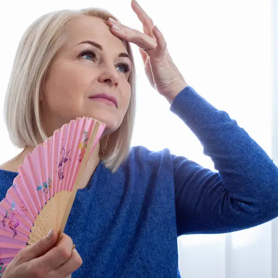 New Zealand woman cooling down beside an open window with iced water during a menopausal hot flush