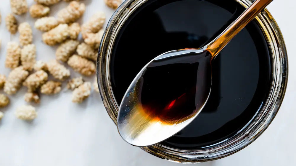 Dark molasses jar on a clean kitchen bench with a simple label detail highlighting unsulphured and sugar cane in the background
