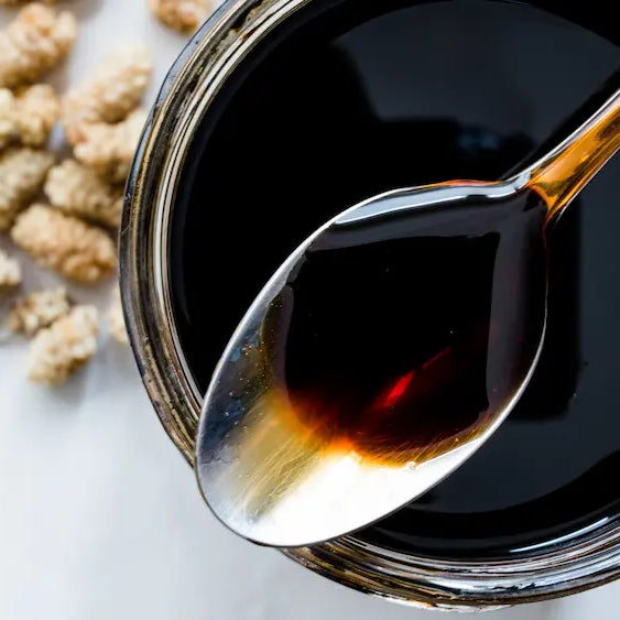 Dark molasses jar on a clean kitchen bench with a simple label detail highlighting unsulphured and sugar cane in the background